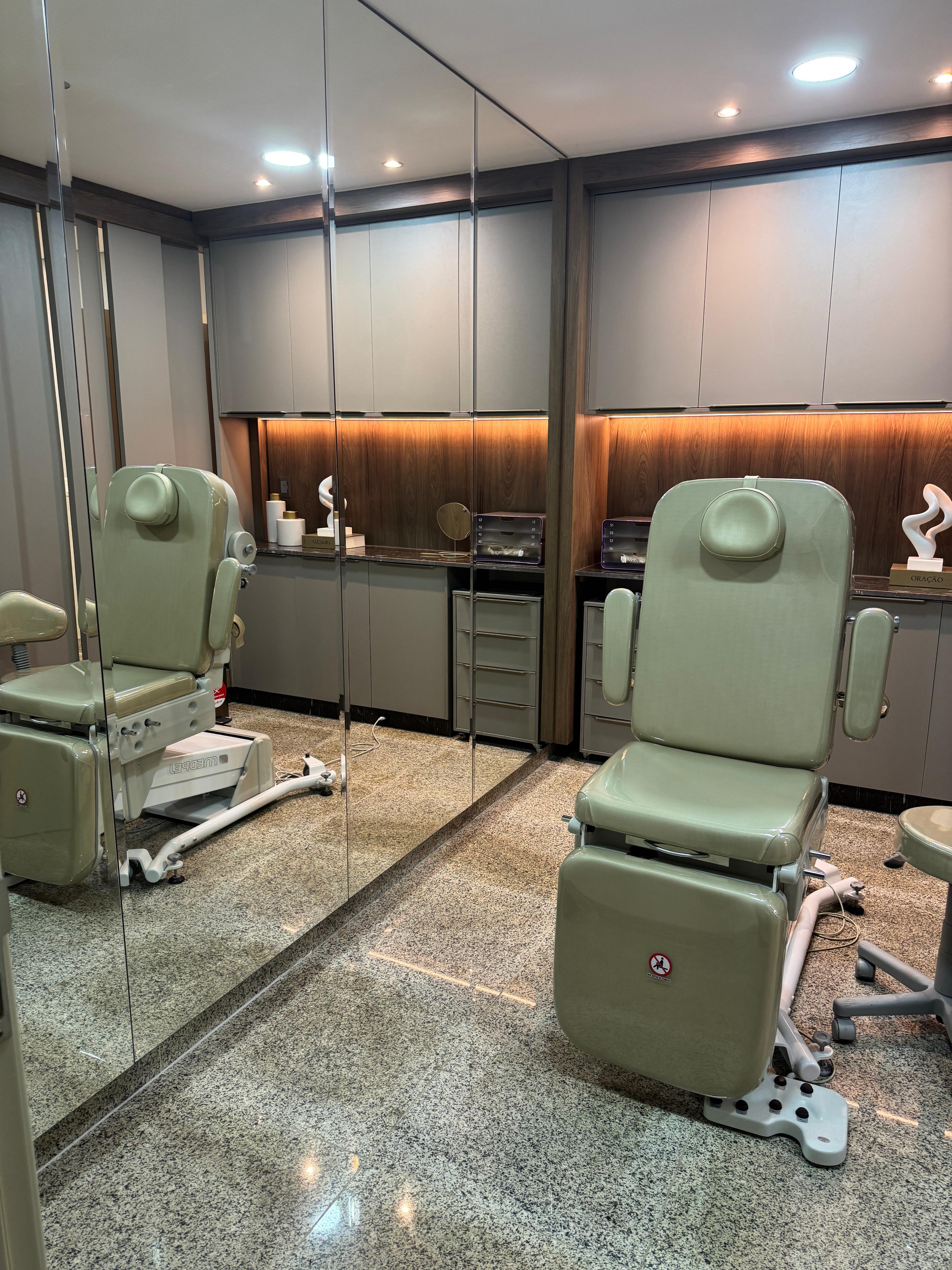 Sala de exame com maca clínica verde-clara, armários e parede espelhada