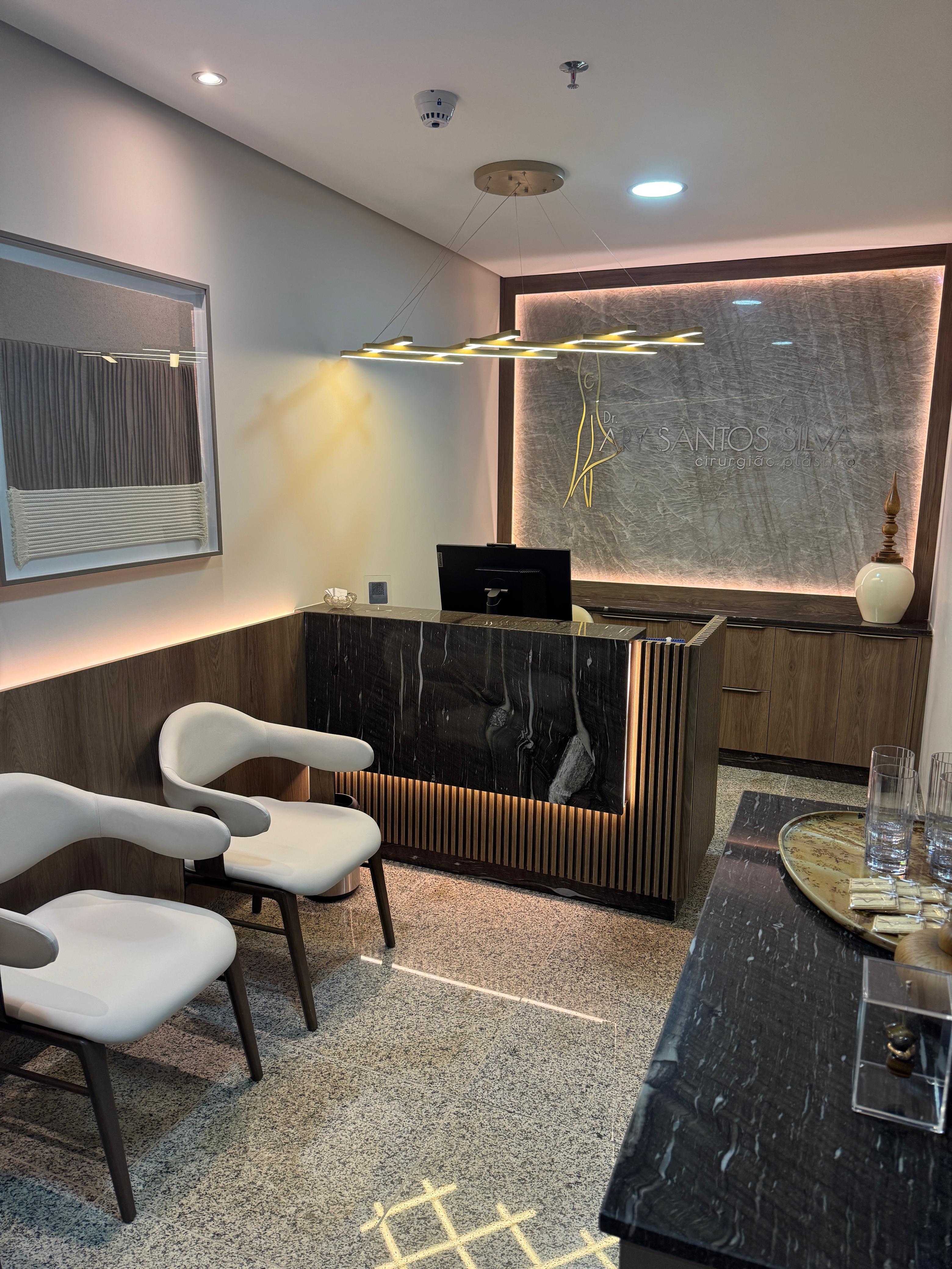 Recepção com balcão de mármore escuro, poltronas claras e iluminação indireta